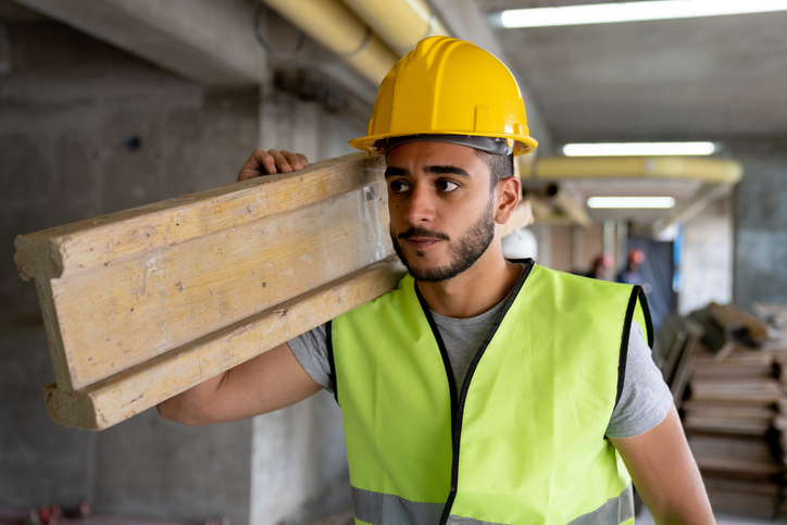 Latin American blue collar worker at a construction site carrying a beam of wood