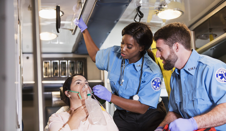 Two multi-ethnic paramedics, a Caucasian man and African-American woman, assisting a patient, giving her oxygen inside an ambulance.
