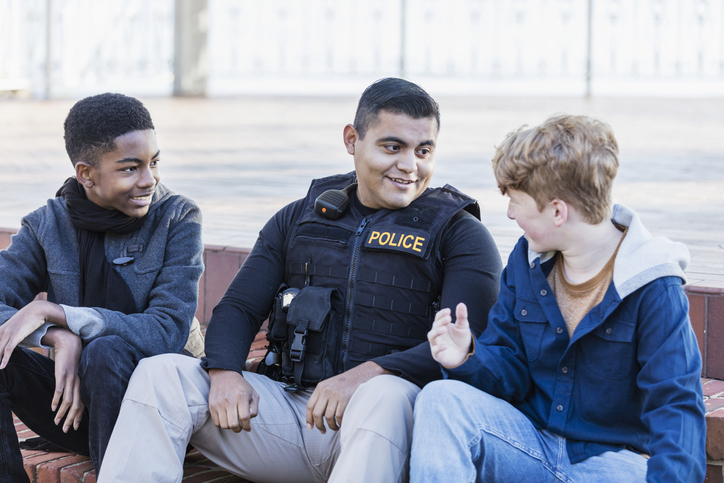 A Hispanic police officer conversing with two adolescents.