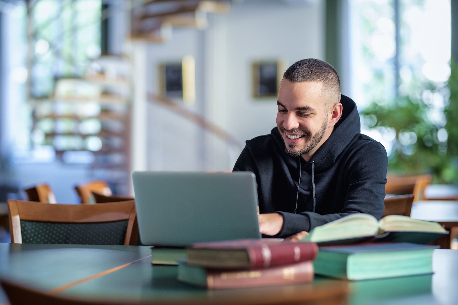 Smiling young man sitting in the university library and learning at a laptop.